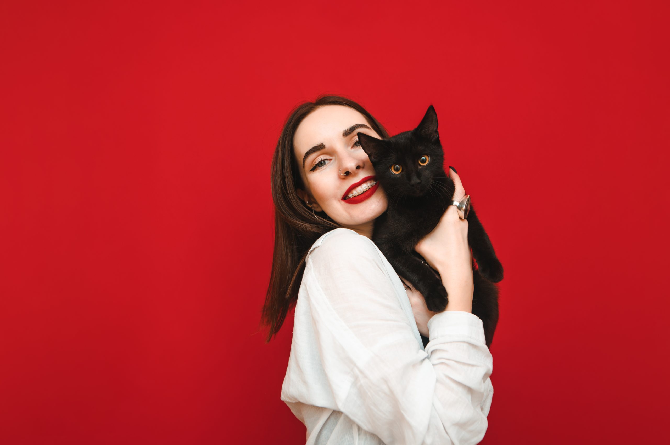 Portrait of a joyful girl hugging with a cute black cat on a red